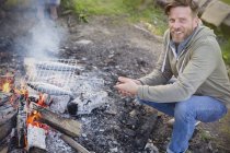 Retrato sorridente homem cozinhando peixe em grill cesta sobre fogueira — Fotografia de Stock