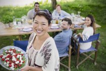 Портрет улыбающейся женщины, подающей капрезский салат друзьям за столом для вечеринок в саду — стоковое фото