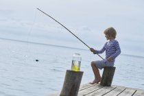 Garçon pêche au large du quai au bord du lac — Photo de stock