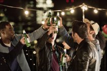 Young men toasting beer bottles at rooftop party — Stock Photo
