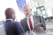 Businessmen talking using digital tablet in airport concourse — Stock Photo