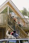 Friends on stairs waving to friends in car outside sunny cabin — Stock Photo