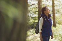 Woman hiking with backpack looking up in woods — Stock Photo