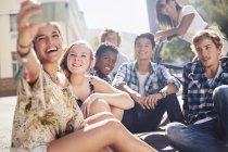 Smiling teenage friends posing for selfie on sunny urban street — Stock Photo