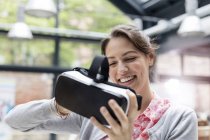 Улыбающаяся женщина пробует очки для симулятора виртуальной реальности на технологической конференции — стоковое фото