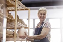 Усміхнена старша жінка розміщує вазу з кераміки на полиці в студії — стокове фото