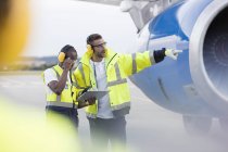 Controladores de tráfico aéreo con portapapeles junto al avión en asfalto del aeropuerto - foto de stock