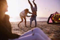 Woman holding man doing handstand on sunset beach — Stock Photo