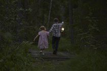 Brother and sister walking with lantern over footbridge in woods — Stock Photo