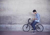 Teenage boy texting on BMX bicycle at wall — Stock Photo