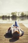 Donna sdraiata rilassante ascoltando musica con le cuffie sul molo soleggiato del lago — Foto stock