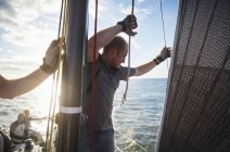 Uomo regolazione vela sartiame su barca a vela — Foto stock
