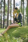 Бігун відпочиває їсть яблуко на моховинній скелі в лісі — стокове фото