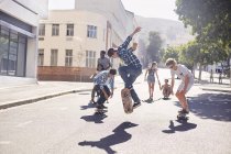Подростковые друзья катаются на скейте на солнечной городской улице — стоковое фото