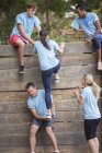 Teamkollegen helfen Frau auf Boot-Camp-Hindernisparcours über Mauer — Stockfoto