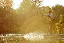 Uomo anziano pesca a mosca a soleggiato lago estivo — Foto stock