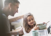 Father and daughter eating breakfast at laptop — Stock Photo