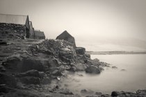 Чорно-біле зображення будинків на скелі над водою — стокове фото