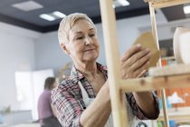 Усміхнена старша жінка розміщує кераміку на полиці в студії — стокове фото