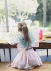 Vue arrière de la fille dans les ailes de fée coloration à la table à manger — Photo de stock