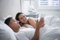 Улыбающаяся пара, лежащая в постели с помощью цифрового планшета — стоковое фото