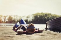 Donna che si rilassa sdraiata sul molo ascoltando musica con le cuffie sul lungolago soleggiato — Foto stock