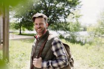 Retrato caminhante sorridente com mochila em bosques ensolarados — Fotografia de Stock
