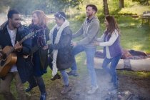 Friends playing guitar dancing in conga line at campsite — Stock Photo