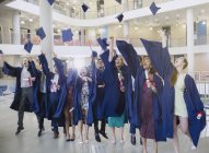 College-Absolventen in Mütze und Kleid werfen Mützen über Kopf — Stockfoto