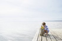 Хлопчик вивчає морські водорості в банці на доці на березі сонячних озер — стокове фото