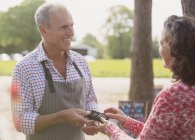 Smiling plant nursery worker offering credit card machine to customer — Stock Photo