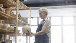 Senior woman placing pottery vase on shelf in studio — Stock Photo