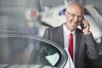 Smiling businessman talking on cell phone in airplane hangar — Stock Photo