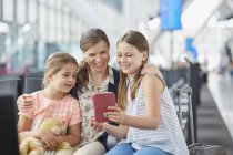 Mother and daughters using digital tablet in airport departure area — Stock Photo
