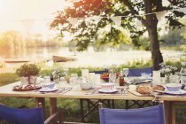 Jardim festa almoço na mesa ao lado do lago idílico — Fotografia de Stock