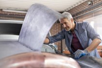 Meccanico guardando sotto il cofano dell'automobile in officina di riparazione auto — Foto stock