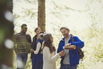 Smiling friends hiking pouring coffee from insulated drink container in woods — Stock Photo