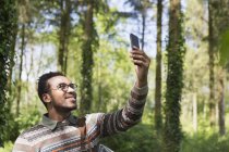 Homme souriant prenant selfie avec téléphone de caméra dans les bois ensoleillés — Photo de stock