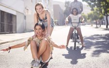 Teenage girls riding skateboard and BMX bicycle on sunny urban street — Stock Photo