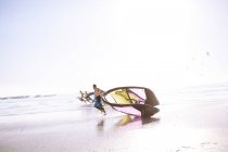 Человек тащит оборудование для кайтбординга по пляжу — стоковое фото