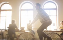 Casual businessman riding bicycle in sunny office — Stock Photo