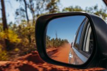 Red clay dust cloud in side-view mirror of car — Stock Photo