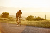 Велогонщик-триатлонист на рассвете на велосипеде по солнечной сельской дороге — стоковое фото