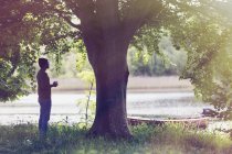 Homme buvant du café sous l'arbre au bord du lac idyllique — Photo de stock