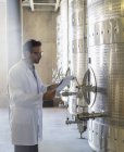 Winzer im Laborkittel mit Klemmbrett überprüft Edelstahlbottich im Weinkeller — Stockfoto