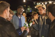 Jovens amigos adultos brindando garrafas de cerveja na festa no telhado — Fotografia de Stock