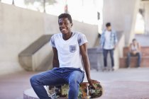 Portrait smiling teenage boy sitting on skateboard at skate park — Stock Photo