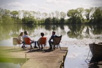 Amigos conversando na ensolarada doca à beira do lago — Fotografia de Stock
