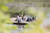 Amigos que ponen y relajan en el muelle soleado al lado del lago - foto de stock