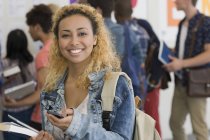 Усміхнена студентка-жінка використовує мобільний телефон з іншими студентами на задньому плані — стокове фото